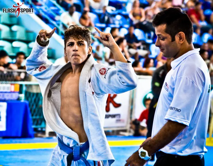 A young competitor in a white gi celebrating on the tournament mat