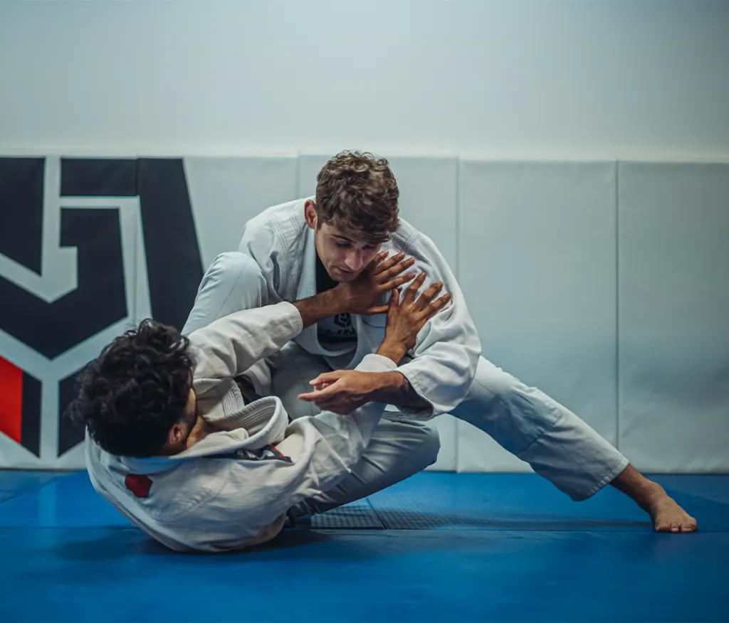 Alexandre Molinaro passing guard in the Gi in front of the academy’s logo wall